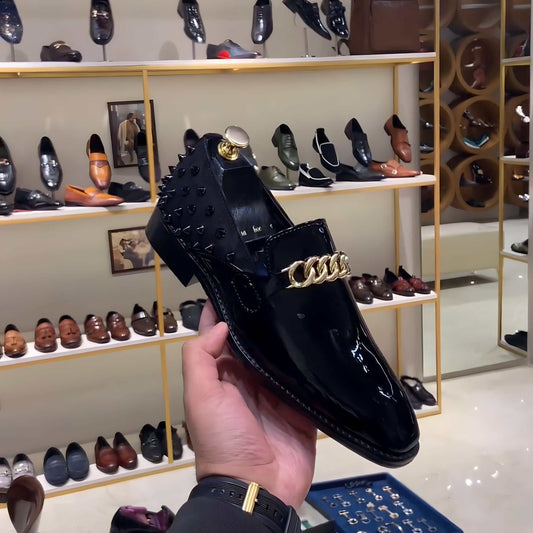 Black studded patent moccasins with gold chain detail held in hand in shoe store