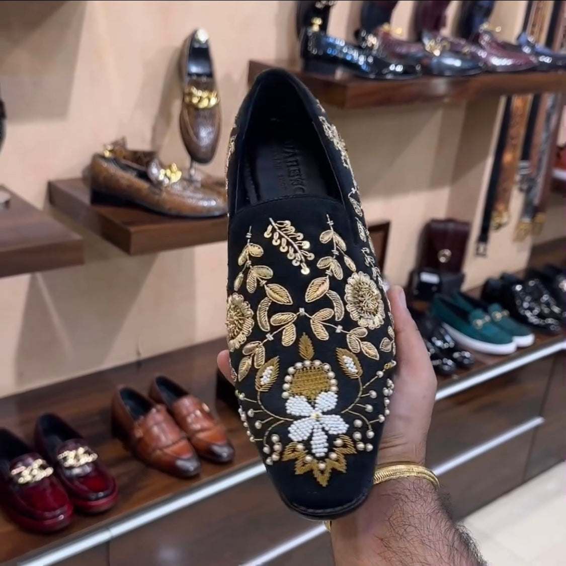 Black hand-embroidered moccasin with gold and white floral design held in hand in shoe store