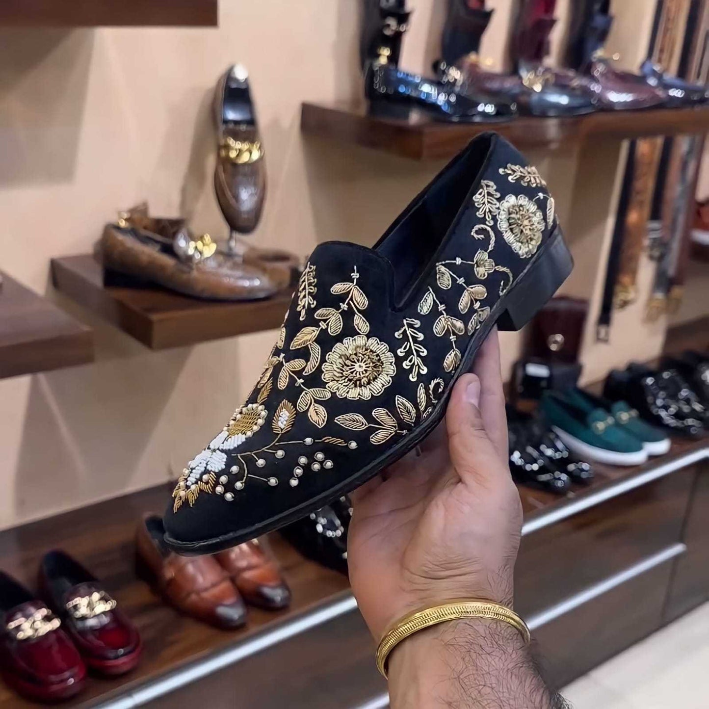 Hand-embroidered black moccasins with gold floral design held in hand in shoe store background