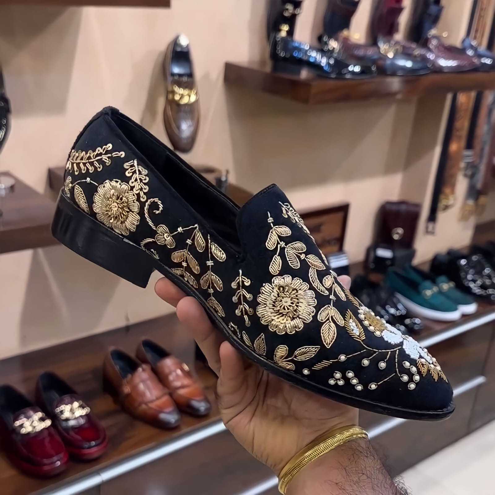 Black hand-embroidered moccasins with gold floral design held in hand in a shoe store