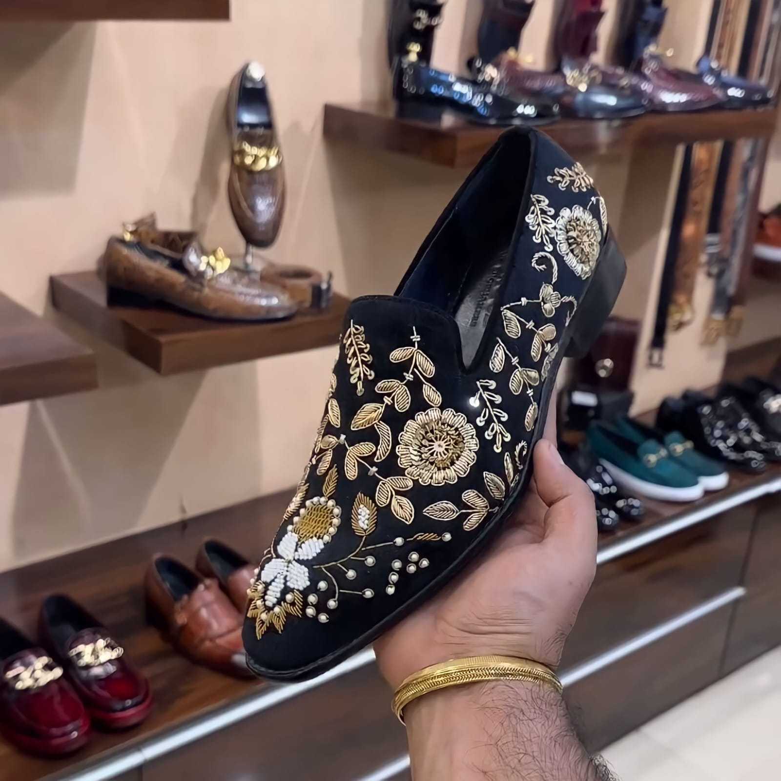 Black hand-embroidered moccasins with gold floral designs held in a store displaying various shoes